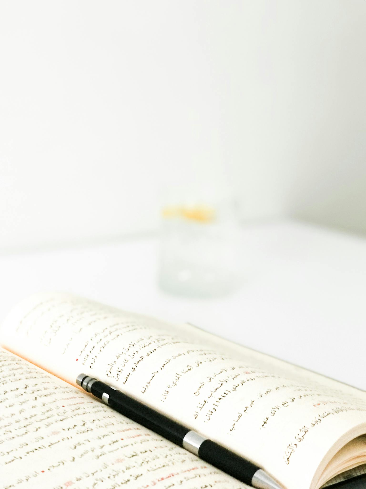Open book with Arabic script and pen on a white table. Minimalist style.